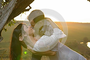 Two sweethearts kissing under tree at sunset