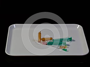 Two syringes and broken ampules in a white plastic dish on dark background