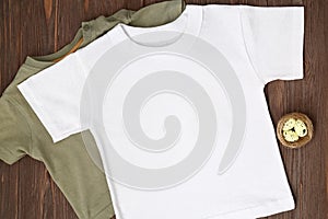 Two t-shirt green and white. Mockup with Easter eggs and nest, flat lay on brown wooden background