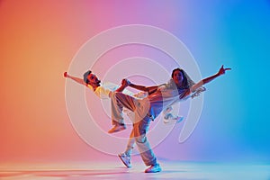 Two talented dancers mid-movement performing in vibrant pink and blue lighting against gradient background. Dynamic