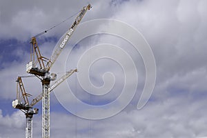 Two tall cranes with cabin against a cloudy blue sky