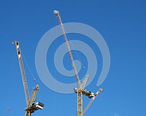 Two tall yellow construction cranes working against a blue sky
