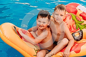 Two tanned happy preschooler boys are sitting on an air mattress in the pool. hot summer