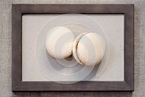 Two tasty macaroons of cream colors in wooden frame, sweet art