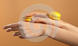 Two tasty yellow dessert macarons on female hands isolated