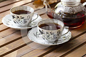 Two tea cups with tea and teapot at wood background