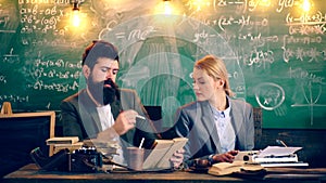 Two teachers are intelligently dressed engaged in a school classroom on the background of a green board. Teacher in