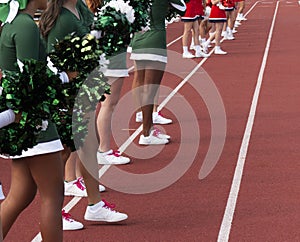 Two teams of cheerleaders standing on the tsideling cheering during football game