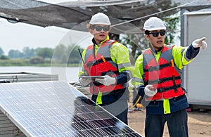 Two technician workers with safety uniform stand beside of solar cell panel and one point forward to discuss about work with his