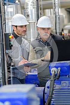 Two technicians with laptop and clipboard checking pump