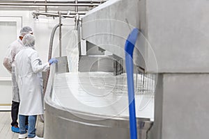 Two technologists standing at  the stainless mixing tank with milk before the fermentation process at the cheese manufacturing