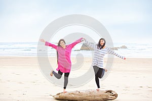 Two teen girls balancing on log at beach