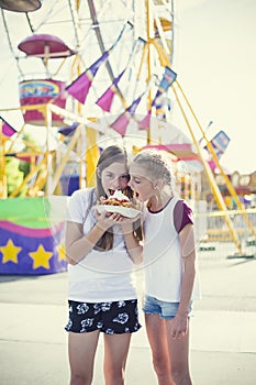 Two teen girls making a silly face while eating a funnel cake at an amusement park ride