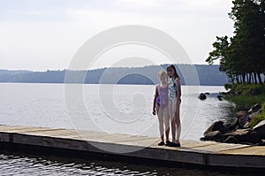 Two teen girls standing on wooden dock with swim suits on in summer with copy space