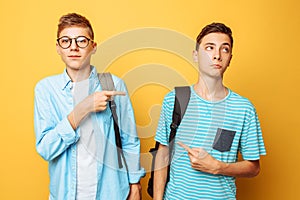 Two teen guys point at each other with their thumbs, blame and do not want to admit their guilt, isolated on a yellow background photo