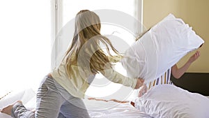 Two teen pyjamas girls having pillow fight on bed. They are laughing to each other.