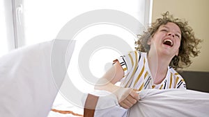 Two teen pyjamas girls having pillow fight on bed. They are laughing to each other.