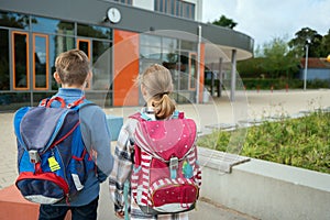 Two teen students with backpacks waiting in front of modern school