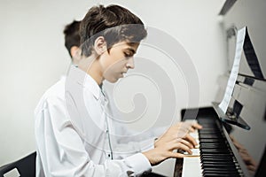 Two teenage boys play piano in class or at home .