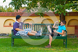 Two teenage boys sitting on the bench and throwing