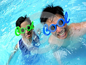 Two teenage boys wearing sunglasses with the word cool for its frame in a swimming pool