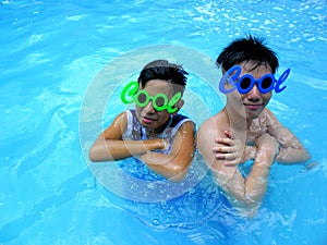 Two teenage boys wearing sunglasses with the word cool for its frame in a swimming pool