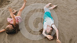 Two teenage children are lie on the beach.