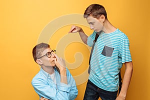 Two teenage friends, one guy humiliates the other, popular humiliates the unpopular, on a yellow background