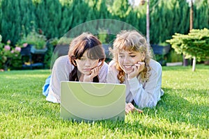 Two teenage girlfriends using laptop lying on grass on sunny summer day