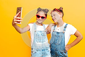 Two teenage girls, girlfriends have a rest and take a selfie on a smartphone on a yellow background