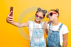 Two teenage girls, girlfriends have a rest and take a selfie on a smartphone on a yellow background