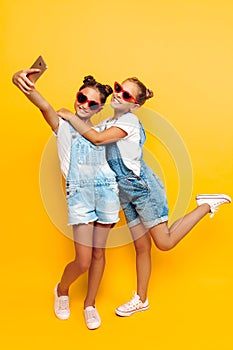 Two teenage girls, girlfriends have a rest and take a selfie on a smartphone on a yellow background