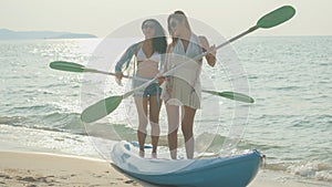 Two teenage girls holding oars and standing dancing on the beach on their summer vacations, smiling and happy on vacation