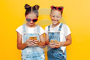 Two teenage girls holding a smartphone in their hands and looking at the screen on a yellow background