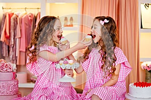 Two teenage girls in pink dresses and long curled hair at a cake party. They try cakes