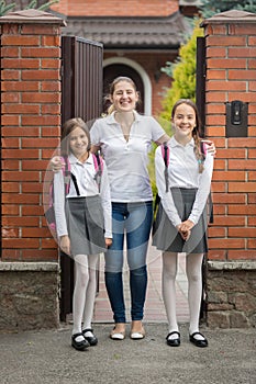 Two teenage girls posing with mother in front of big house before going to school