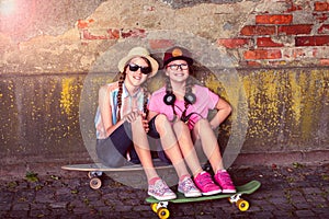 Two teenage girls sitting on a skateboard and smiling