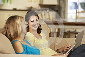 Two Teenage Girls Sitting On Sofa At Home Using Tablet Computer And Laptop