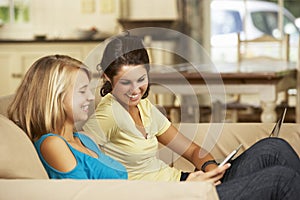 Two Teenage Girls Sitting On Sofa At Home Using Tablet Computer And Laptop