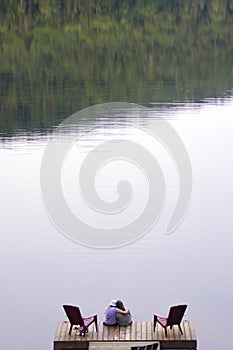 Pair of teenage girls sitting on wooden dock at lake with copy space