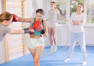 Two teenage girls in sportswear are engaged in boxing sparring in the gym under guidance of trainer in gym