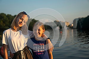 Two teenage girls stand on the shore of the lake at sunset. friendship concept