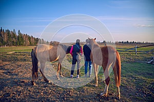 Two teenage girls stand with their backs to the camera and hold the reins of young horses.