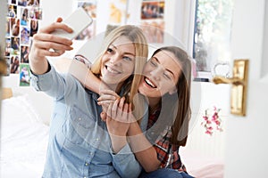 Two Teenage Girls Taking Selfie In Bedroom At Home