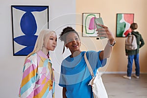 Two teenage girls taking selfie photo in art gallery