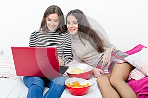 Two teenage girls using notebook and eating snacks while sitting