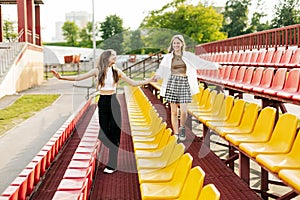 Two teenage girls walk together through the stands of the school stadium, talking, holding hands, best friends return