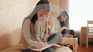 Two teenage sister doing homework and writing in copybooks. Teens studying