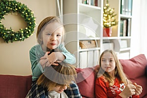 Two teenage sisters and their toddler brother snuggling up on the sofa in a cozy living room at Christmas. Cute children having