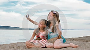 Two teenage are sitting on a sandy beach, on the Internet in phone.